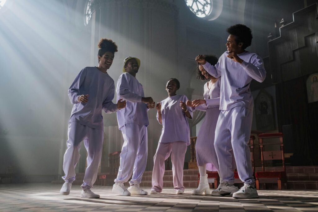 A group of people joyfully singing and dancing in a sunlit church interior with sunbeams highlighting the scene.